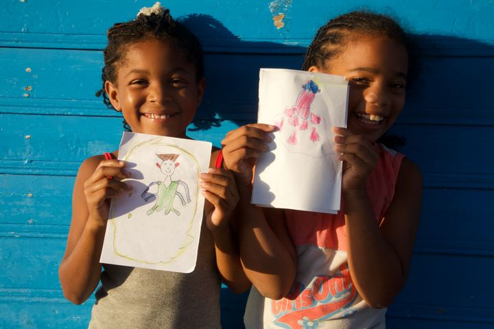 Two girls holding their aliens against a blue wall, Barú